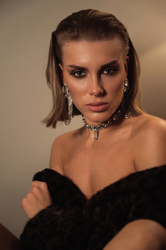 Blonde / A blonde woman with beautiful eyes, wearing jewelry and a fur coat over her bare body, is looking at the camera.