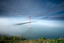 Amo- te , Lisboa! / The 25 de Abril Bridge (Ponte 25 de Abril - &quot;25th of April Bridge&quot;), is a suspension bridge connecting the city of Lisbon, capital of Portugal, to the municipality of Almada on the left (south) bank of the Tejo river. It was inaugurated on August 6, 1966 and a train platform was added in 1999. Because of its similar coloring, it is often compared to the Golden Gate Bridge in San Francisco, USA. In fact, it was built by the same company (American Bridge Company) that constructed the San Francisco-Oakland Bay Bridge and not the Golden Gate, also explaining its similarity in design. With a total length of 2,277 m, it is the 20th largest suspension bridge in the world. The upper platform carries six car lanes, the lower platform two train tracks. Until 1974, the bridge was named Salazar Bridge (Ponte Salazar).